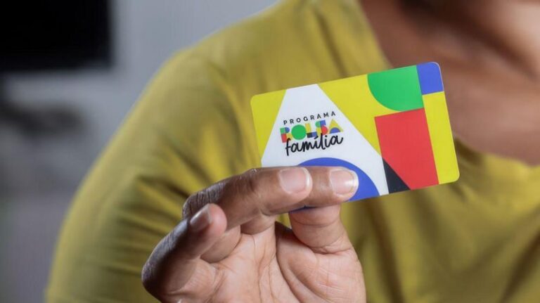Imagem com foco na mão de uma mulher segurando o cartão do programa social, Bolsa Família.